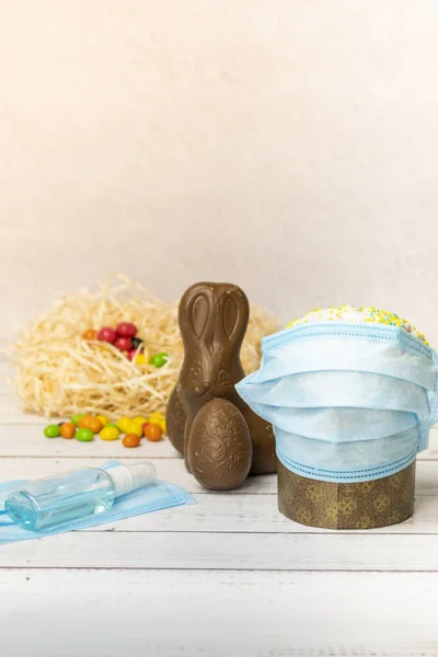 Easter cake in protective medical face mask and chocolate eggs with antiseptic, close-up. Protection against viruses. The concept of the celebration of Holy Easter 2020 during coronavirus pandemic