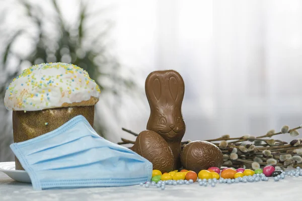 Easter cake, protective medical face mask and chocolate eggs and rabbit, close-up. Protection against viruses. The concept of the celebration of Holy Easter 2020 during coronavirus pandemic