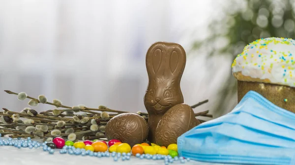 Easter cake, protective medical face mask and chocolate eggs and rabbit, close-up. Protection against viruses. The concept of the celebration of Holy Easter 2020 during coronavirus pandemic