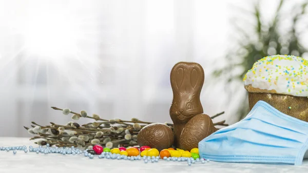 Easter cake, protective medical face mask and chocolate eggs and rabbit, close-up. Protection against viruses. The concept of the celebration of Holy Easter 2020 during coronavirus pandemic