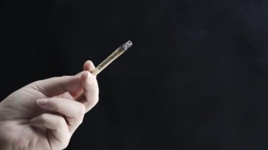 Tıbbi marihuana esrarını tutan ve siyah arka planda sigara içen bir kadının yakın çekimi, yavaş çekim. Esrar bir bitkisel veya alternatif tıp kavramıdır.