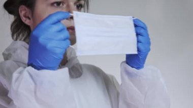 Koruyucu kıyafetli genç bir kadın doktorun ameliyat maskesi ve portresi taktığı yakın plan. Sağlık, hastane veya klinik ve koronavirüs salgını kavramı 