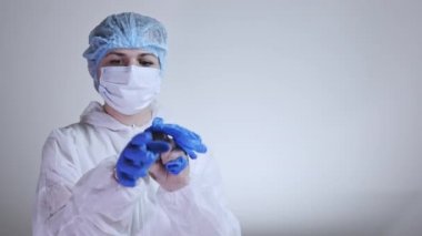 Koruyucu giysili genç bayan doktorun ameliyat eldivenleri giydiği yakın plan. Sağlık, hastane veya klinik ve koronavirüs salgını kavramı 