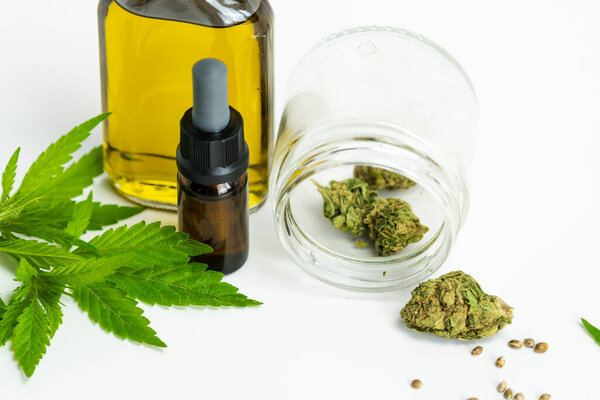 Стеклянные бутылки с эфирным маслом CBD, медицинские листья марихуаны, почки и семена на белом фоне, крупный план. Концепции альтернативной или травяной медицины, косметики CBD масло
.