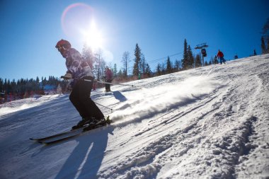Renkli ceketli ve siyah pantolonlu kayakçı aşağı geliyor.