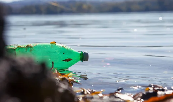 A green plastic bottle floats down the river. The river is very