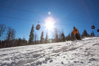 Dağda güneşli bir sabah, kayak yamacında çok kayakçı yok. Teleferik kayak pistinin hemen üstünde ve çam ormanı her yerde..