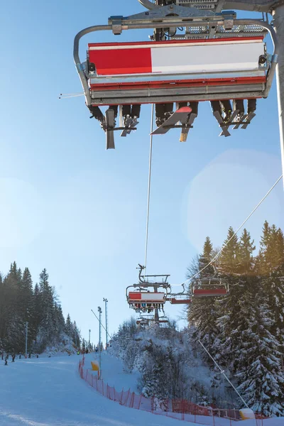 滑雪者的腿在滑雪车上的选择焦点 阳光照亮了六座滑雪车 缆车下面有一个滑雪场 滑雪场和一片松树林 — 图库照片