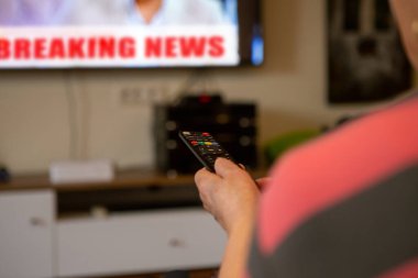 Son sınıf öğrencisi bir kadın televizyon seyrediyor. Kanalı değiştirmek istediği için televizyonu işaret ettiği uzaktan kumandayı elinde tutuyor. Odak noktası uzaktan kumanda..