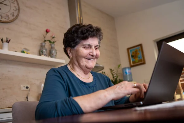 Siyah kısa saçlı son sınıf öğrencisi bir kadın bir masada oturuyor ve dizüstü bilgisayarda çalışıyor. İnternette yeni yemek tarifleri arıyor ve düşünceli ve gülüyor..