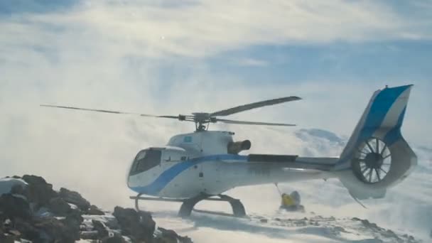 Elicottero elisciante atterrato sulle montagne innevate, sollevando una grande nuvola di neve — Video Stock