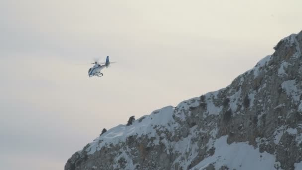 De helikopter vliegt tegen de achtergrond van een rotsachtige besneeuwde berg — Stockvideo