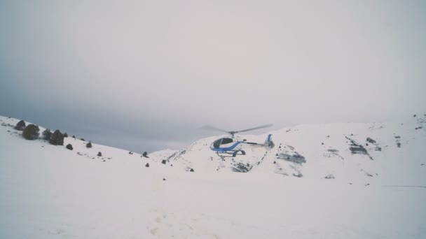 Un hélicoptère blanc à l'arrière-plan ciel nuageux atterrit dans les montagnes de neige — Video