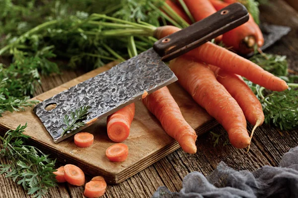 Fresh carrots with tops cut into a beautiful big knife.   The ingredients for the salad. Health and diet food. All on an old wooden table in rustic style.