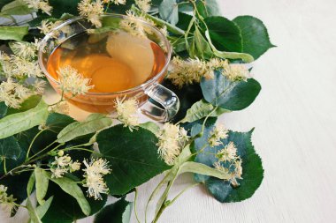 Bir bardak yeşil çay ve ıhlamur çiçekleri. Soğuk algınlığı ve enfeksiyonlar için vazgeçilmez bir tedavi. Beyaz ahşap arka plan. Yukarıdan manzara. Uzayı kopyala Yatay