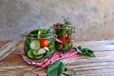 Kahverengi ahşap bir masada dereotlu iki cam kavanozda salatalık ve domates turşusu. Evi koruma, fermantasyon vejetaryen yemeği, organik gıda, kışa hazır..