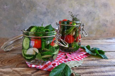 Kahverengi ahşap bir masada dereotlu iki cam kavanozda salatalık ve domates turşusu. Evi koruma, fermantasyon vejetaryen yemeği, organik gıda, kışa hazır..