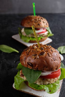 Domatesli vejetaryen hamburger, marul, soğan, fasulye pirzolası ve koyu arkaplanda tahıllı çörek. Her zamanki hamburgerin alternatifi. Sağlıklı beslenme kavramı. Dikey. 