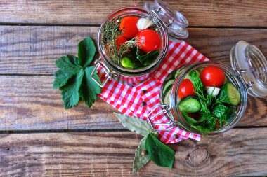 Kahverengi ahşap bir masada dereotlu iki cam kavanozda salatalık ve domates turşusu. Evi koruma, fermantasyon vejetaryen yemeği, organik gıda, kışa hazır. Üst görünüm.