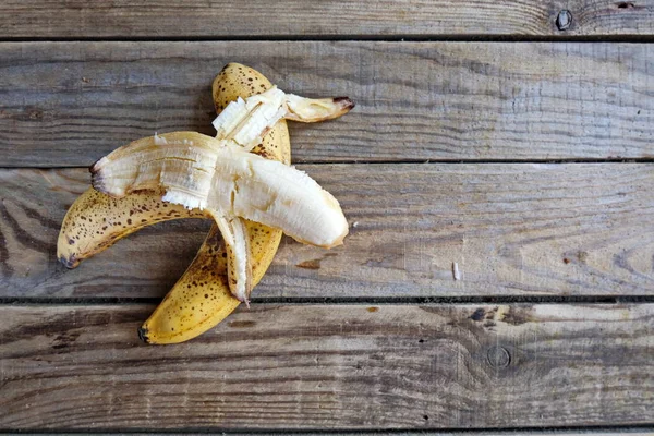 Overripe bananas with dark spots on the skin.   One peeled banana and one unpeeled overripe blackened ugly bananas on  wooden  background. horizontal? copy space.