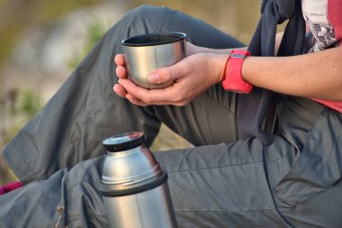 Termoslu bir turist. Kadın doğaya çay döker. Kayadaki kız.