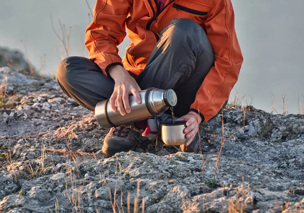 Termoslu bir turist. Kadın doğaya çay döker. Kayadaki kız.