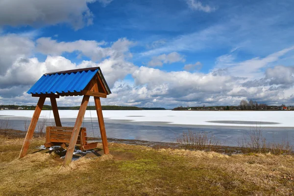 Качели на берегу замёрзшего озера в солнечный весенний день — стоковое фото