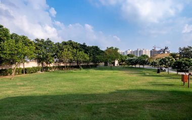 Binalara karşı geniş bir park manzarası ve arkada bulutlu bir gökyüzü.