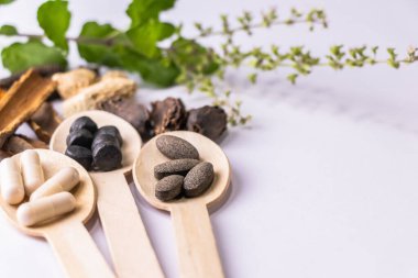 Ayurvedic tıp konsepti. Ayurvedic ilaç tabletlerinin ve kapsüllerin yakın plan çekimleri, beyaz arka planda çeşitli Hint baharatları ve tütsüleriyle ahşap kaşıklarda.