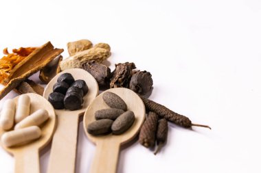 Beyaz arka planda çeşitli Hint baharatlarıyla üç tahta kaşıkta ayurvedik tablet ve kapsüllerin yüksek açılı yakın çekim görüntüleri. Ayurvedic ve Unani tıp danışmanları