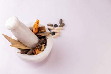 Fotokopi alanı olan beyaz bir zemine tüm baharatlarla ve dağınık bitkisel tabletlerle bir havan topuzunun üst görüntüsü. Bitkisel ve Unani tıp danışmanları