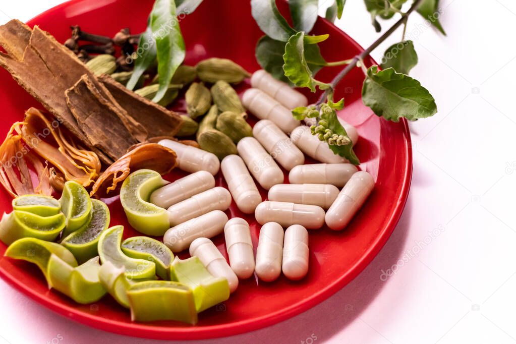 Herbal medicine concept. Close-up of assorted Indian Spices with herbal capsule, green ocimum leaves and sliced aloe vera in a plate on white background