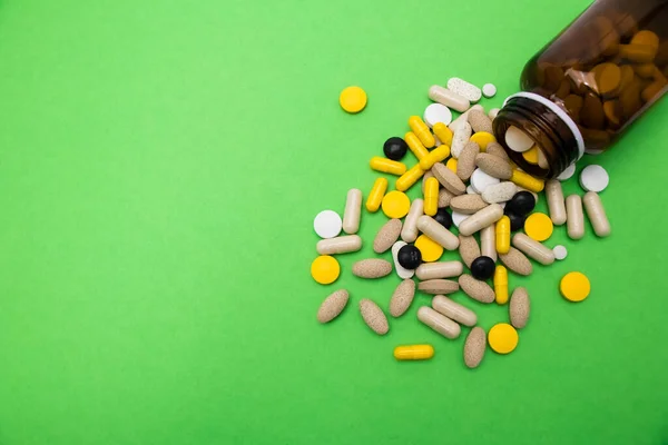 A close up of a bunch of pills coming out of a dark brown bottle with a green space background