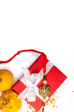 Hint festivali - Kırmızı hediye kutusundaki zarif Rakhi manzarası üzerine serpiştirilmiş pirinç, kumkum ve haldi ve beyaz arka planda tatlılar
