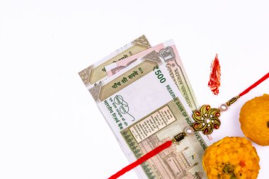 Raksha Bandhan Concept - Geleneksel Hint bilekliği, pirinç taneli ve kumkum markalı tatlılar ve beyaz arka planda Hint para birimi