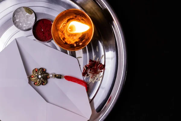 Hint Festivali kavramı. Siyah arka planda pirinç taneleri, kumkum ve diya içeren beyaz bir zarfın içinde Rakhi.