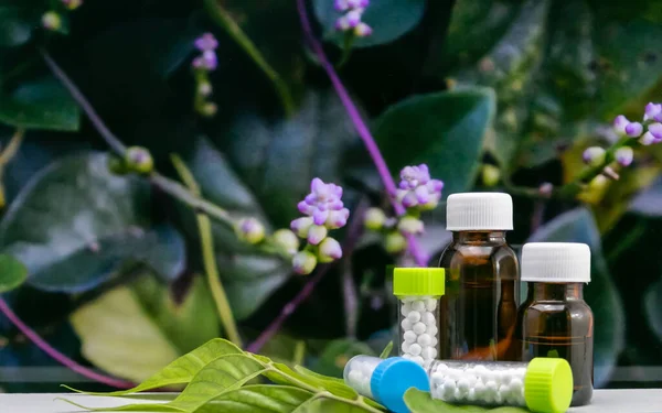 Yapraklı arka planda Homeopati şeker toplarının ve sıvı ilaçların yakın plan çekimi.