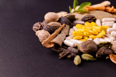 Siyah arka planda sarı bitkisel kapsüller, tabletler ve doğal otlar fotokopi alanı ile yakın çekim. Bitkisel ilaçlar ve sağlıklı bitkiler konsepti