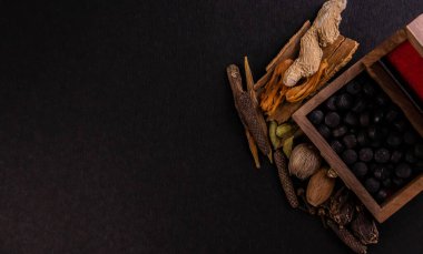 Kara ayurvedik tabletlerin siyah arka planda çeşitli baharatların bulunduğu ahşap bir kutunun üst görüntüsü. Ayurvedik kavram