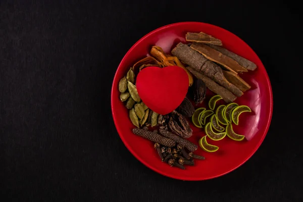 Heart health concept. One red heart shape toy placed between natural herbs and spices in a plate with sliced aloevera and cinnamon sticks