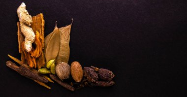 Aromatik bitkiler konsepti. Tarçın, kuru zencefil, gürz, defne yaprağı, uzun biber, yeşil ve siyah kakule, hindistan cevizi, hindistan cevizi, karanfil, siyah arka plana saçılmış.