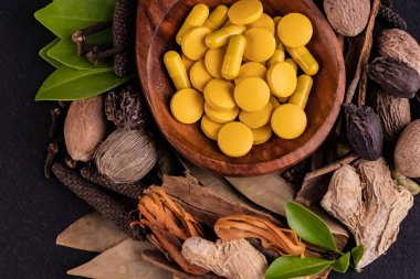 Alternatif tıp konsepti, sarı ayurvedik ilaçların yakın plan çekimi tahta kaşıkta ve siyah arka planda farklı otlar.