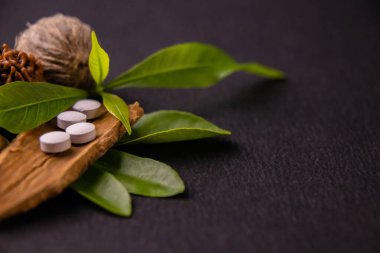 Beyaz ayurvedik tabletlerin siyah arka planda ve kurutulmuş otlar üzerinde makro çekimi, doğal ilaç konsepti