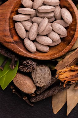 Üst görünüm yeşil yapraklı, hindistan cevizli ve siyah arka planlı diğer otlarla servis kaşığında bitkisel ilaçların toplanması, unani tıp konsepti