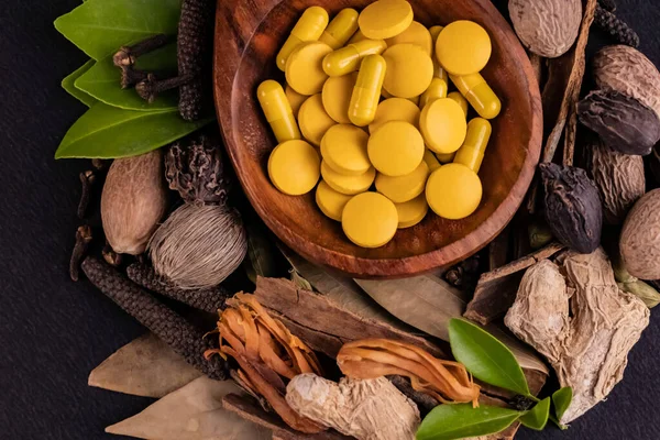 Alternatif tıp konsepti, sarı ayurvedik ilaçların yakın plan çekimi tahta kaşıkta ve siyah arka planda farklı otlar.