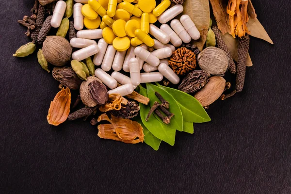 Doğal tıp konsepti, dağınık bitkiler, baharatlar ve siyah arkaplan üzerine ayurvedic tabletler.