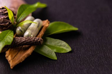 İki bitkisel kapsülün benzersiz makro çekimi, uzun biber ve yeşil otlar fotokopi alanı, ayurveda ve bitkisel konsept ile siyah zemin üzerinde