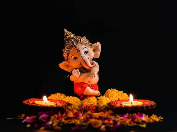 Çiçekli muhteşem Ganesha heykelinin önü ve siyah arka planda iki toprak lambası. inanç kavramı