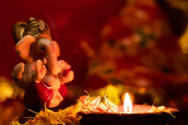 Bulanık arka planda çözünmüş ganesha heykeli ile çiçek yaprakları üzerinde parlayan diya. Hinduizm ve inanç kavramı