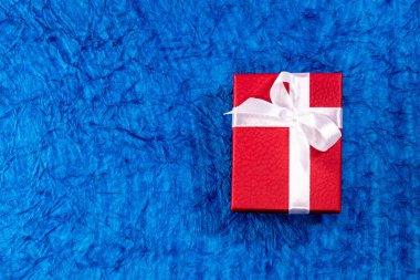 Mavi arka planda beyaz fiyonklu dikey kırmızı hediye kutusunun üst görüntüsü. Evlilik hediyeleri konsepti